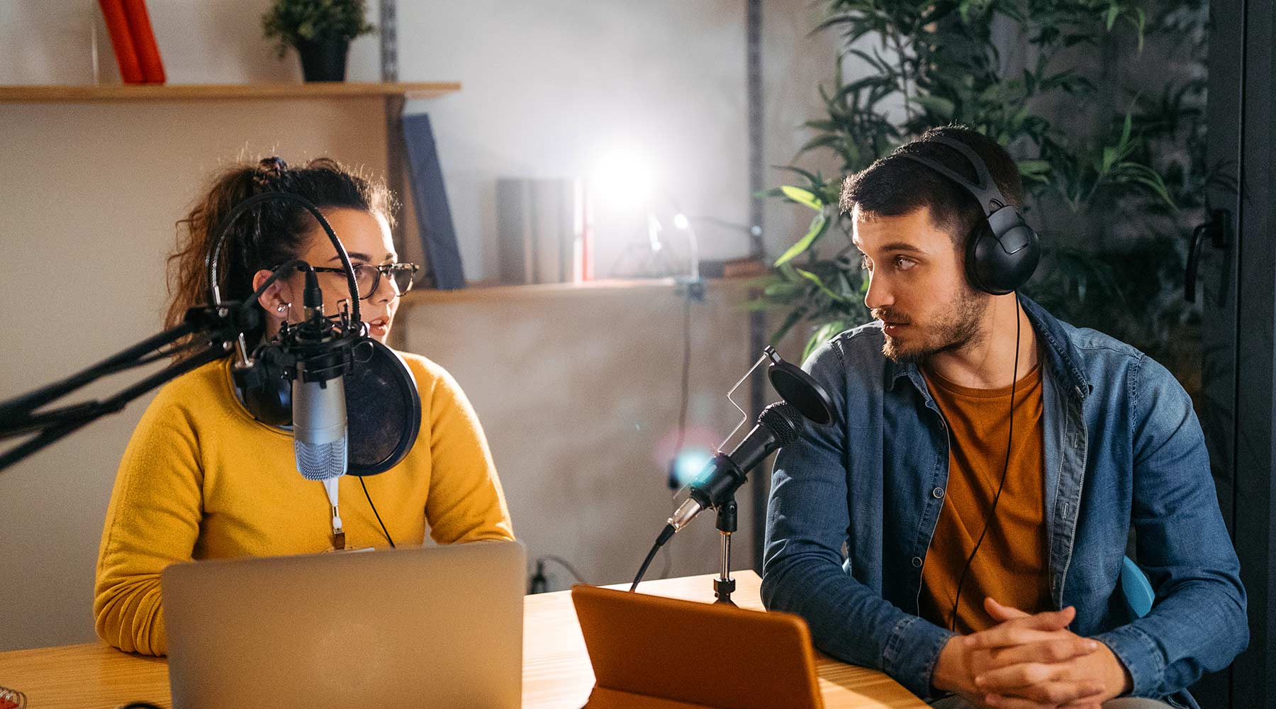 A man and women discuss into microphones while looking at computer screens